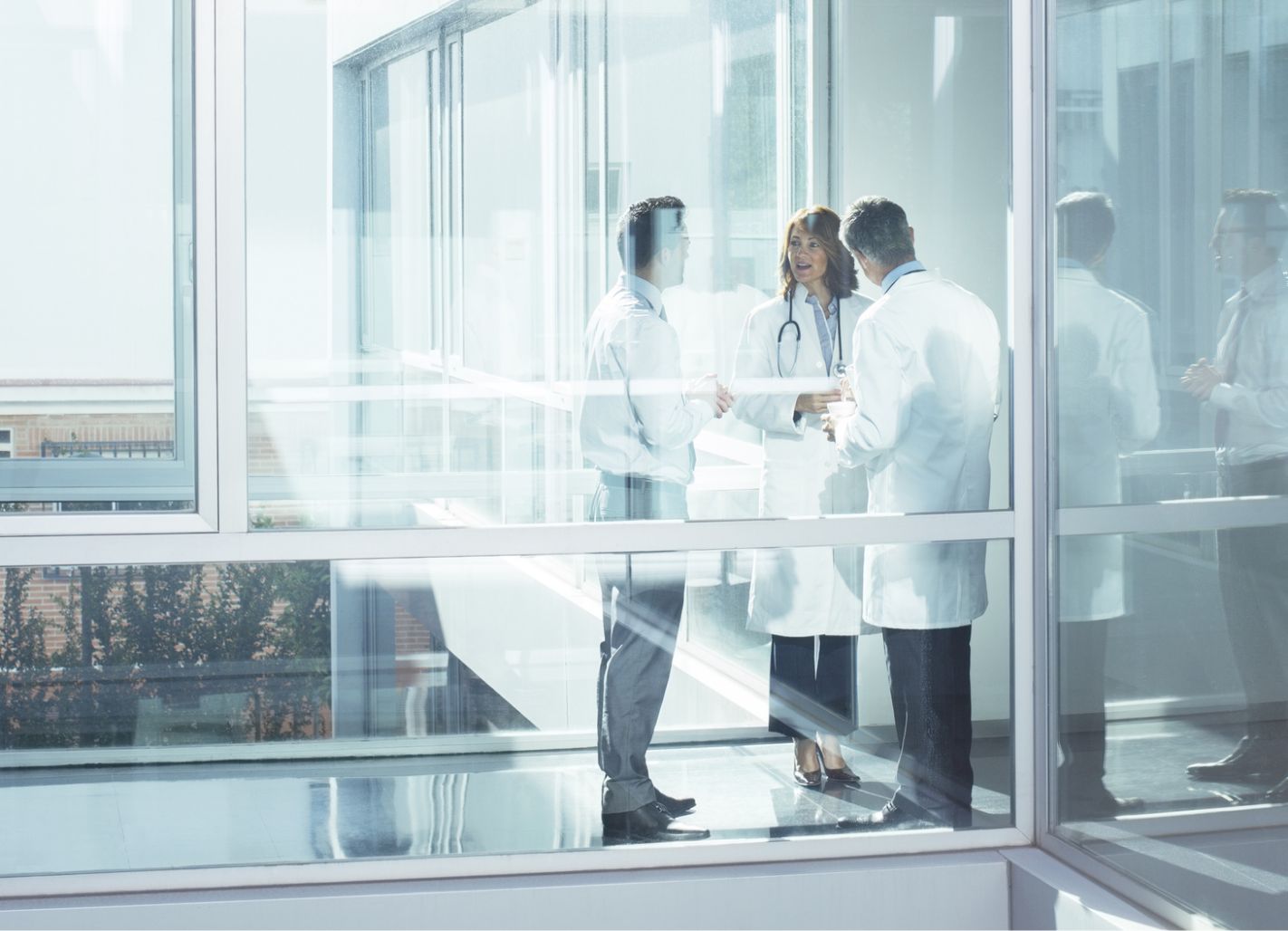 Doctors speaking with and administrator behind a glass windowed walkway.